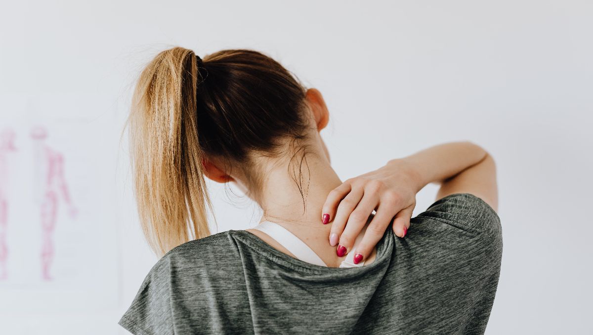 A woman facing back while holding her upper back indicating back pain.
