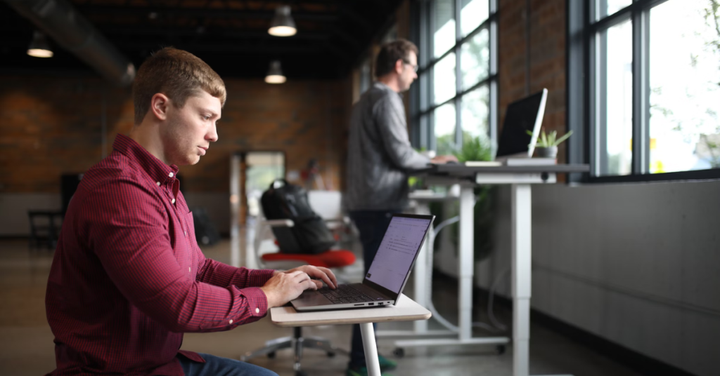 Man sitting on an ergonomic chair and other man working on a standing chair.