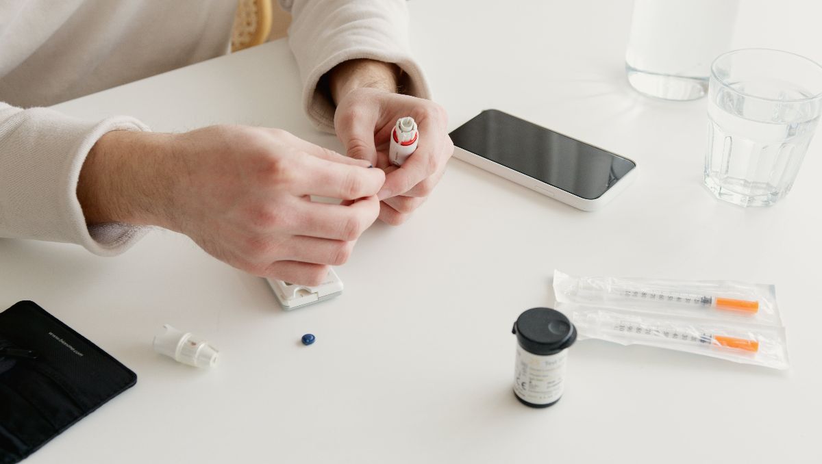 A man holding an injectable, with syringes and medicine in front of him.