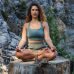 Woman sitting Indian style on a big log, demonstrating posture and health advantages