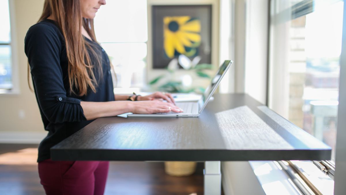 A woman in black shirt working at a standing desk with a laptop.