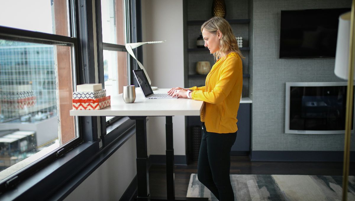A woman wearing yellow shirt and black pants working on a standing desk.