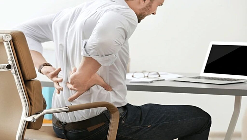is standing better than sitting A man holding his back indicating back pain while sitting in an office chair.