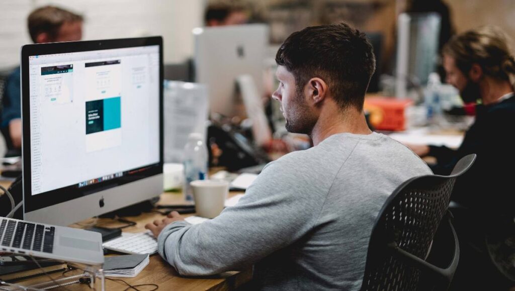 A man in gray sitting at the office desk, working on the desktop.