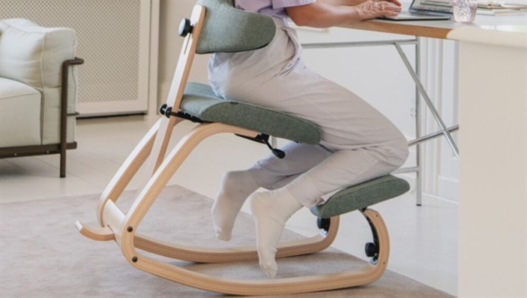 A woman working on her desk while sitting on a kneeling chair.