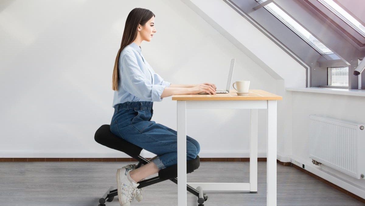A woman working at a desk using a kneeling chair.