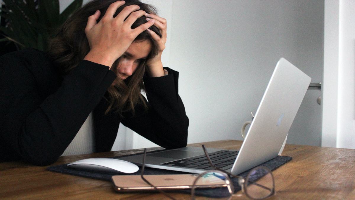 A woman holding her head out of frustration while looking at the laptop.