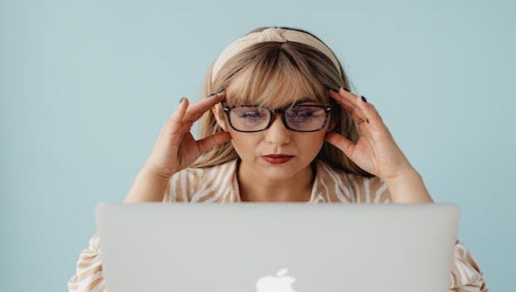 A woman holding her head while facing the laptop.