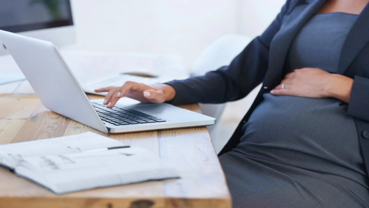 A pregnant woman sitting in an office chair while working on her laptop.