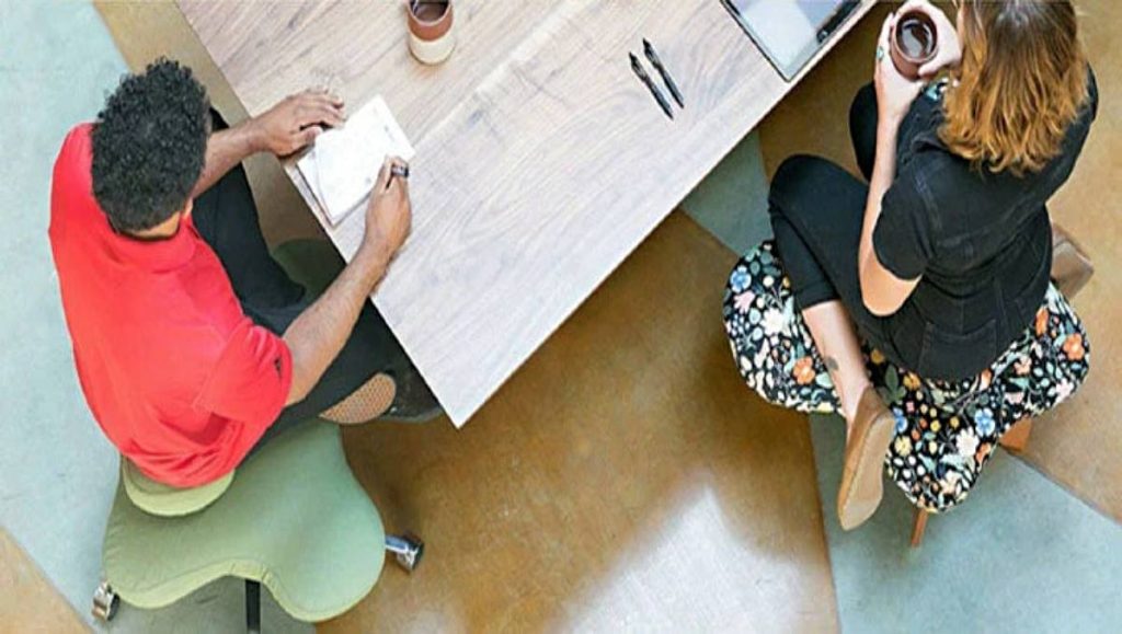 Two office workers sitting on a cross legged office chair