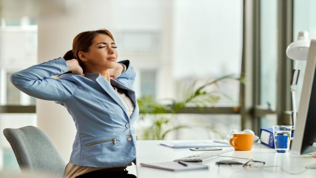 Young woman with eyes closed stretching while working at her office desk