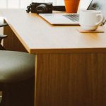 A wood office desk with laptop and cup above