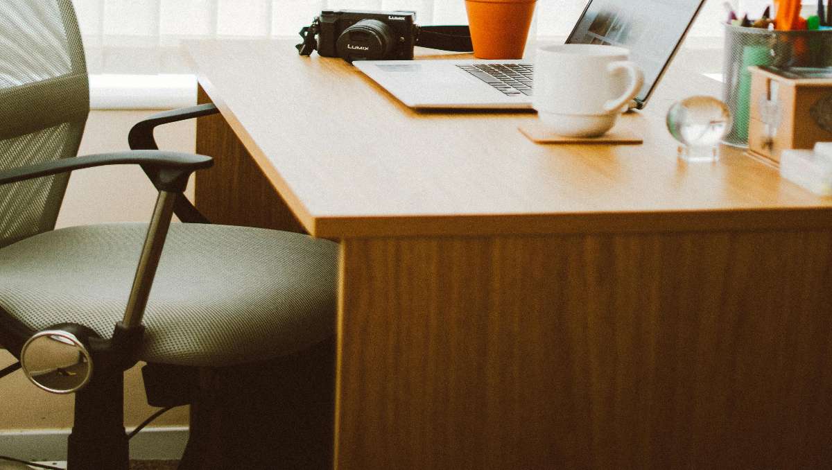 A wood office desk with laptop and cup above