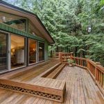 A wooden outdoor deck in a green house with trees