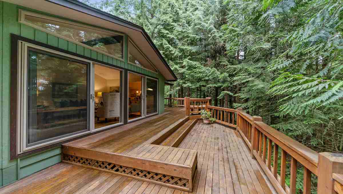 A wooden outdoor deck in a green house with trees
