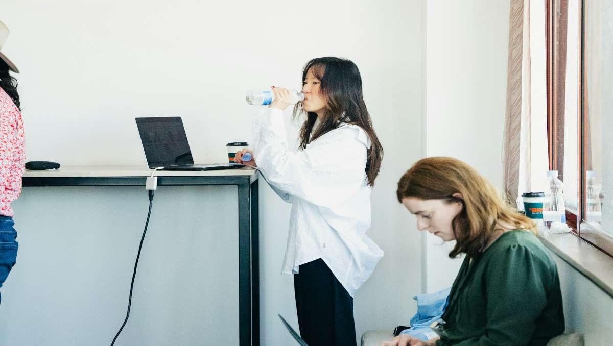 Woman drinking water while working on a standing desk